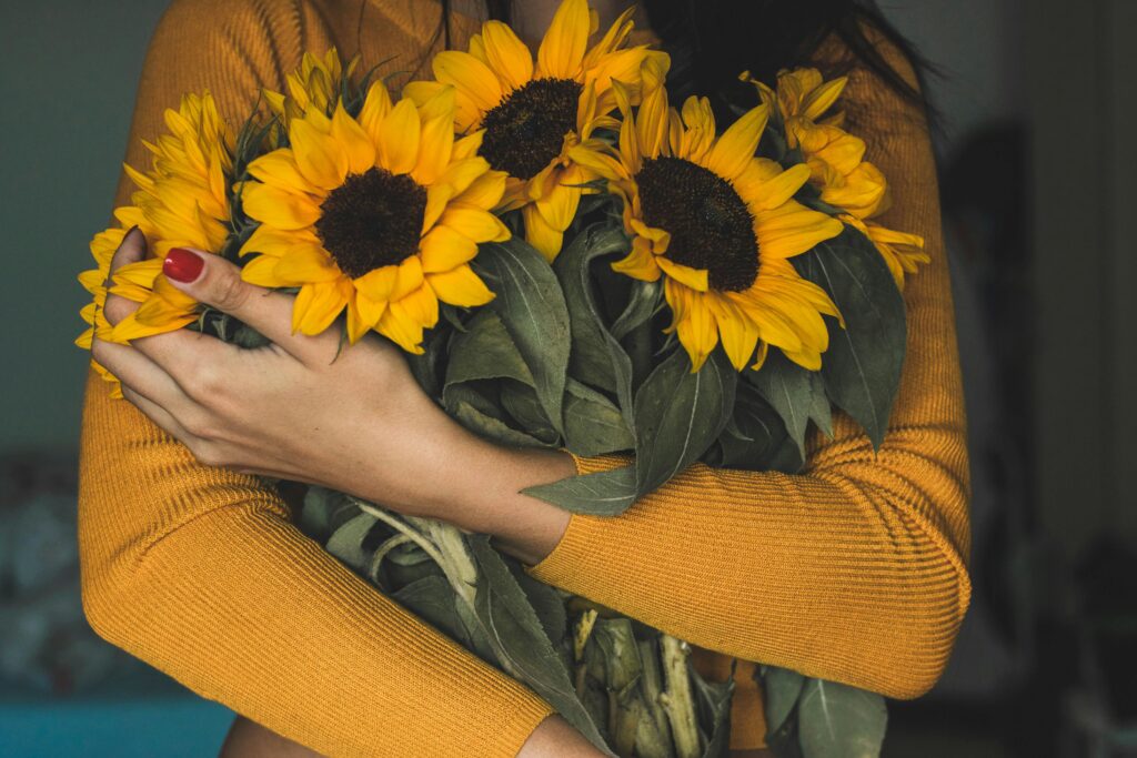 A woman in a yellow sweater holds vibrant sunflowers, capturing a warm, cozy atmosphere.