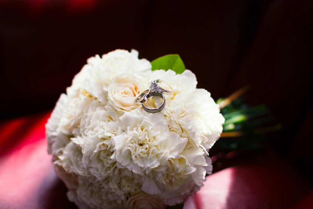 Close-up of wedding rings on a white carnation bouquet, symbolizing love and marriage.