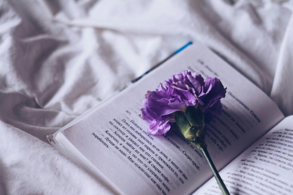 A close-up of a purple carnation flower resting on an open book, symbolizing romance and knowledge.