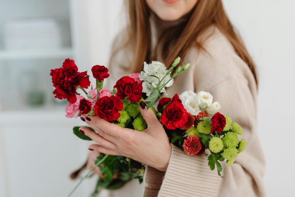 A woman in a beige sweater holds a vibrant bouquet of flowers indoors.