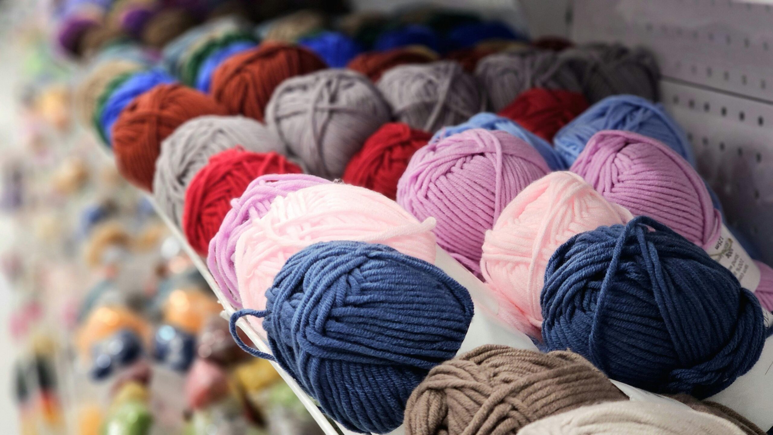 Vibrant yarn balls in a variety of colors neatly arranged on a store shelf.
